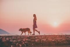 Une femme promenant son chien sans laisse sur fond de coucher de soleil