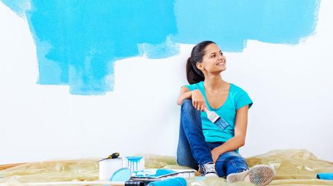 Jeune femme peignant un nouvel appartement rénové avec de la peinture.