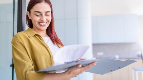 Une jeune femme aux cheveux roux sourit, tout en feuilletant un dossier au format papier