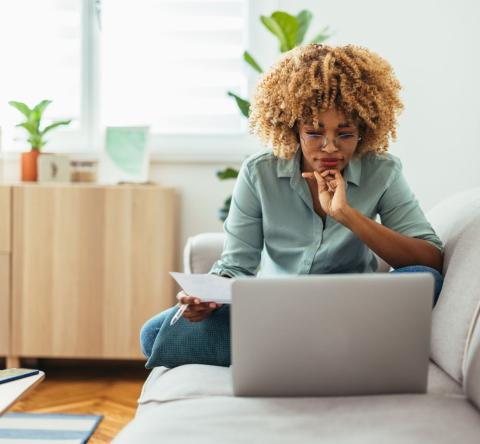 Jeune femme sur son canapé se renseigne son ordinateur pour bien choisir son syndic