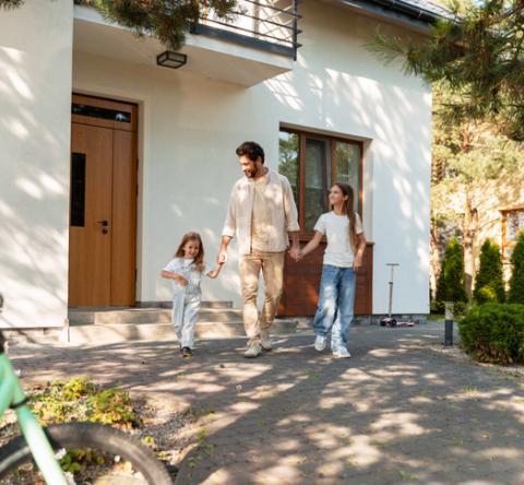 Père avec ses deux filles, devant leur maison familiale blanche, à étage.  